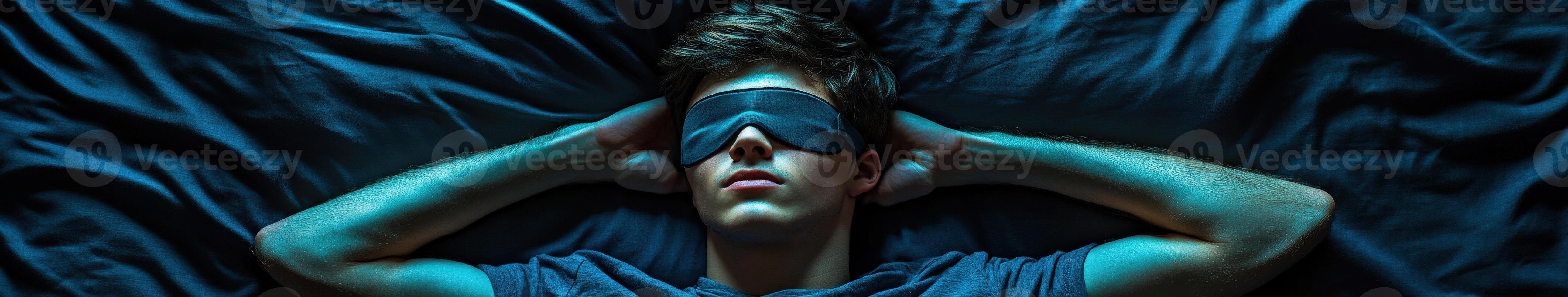 Young man relaxing in bed with sleep mask at night in dark environment photo