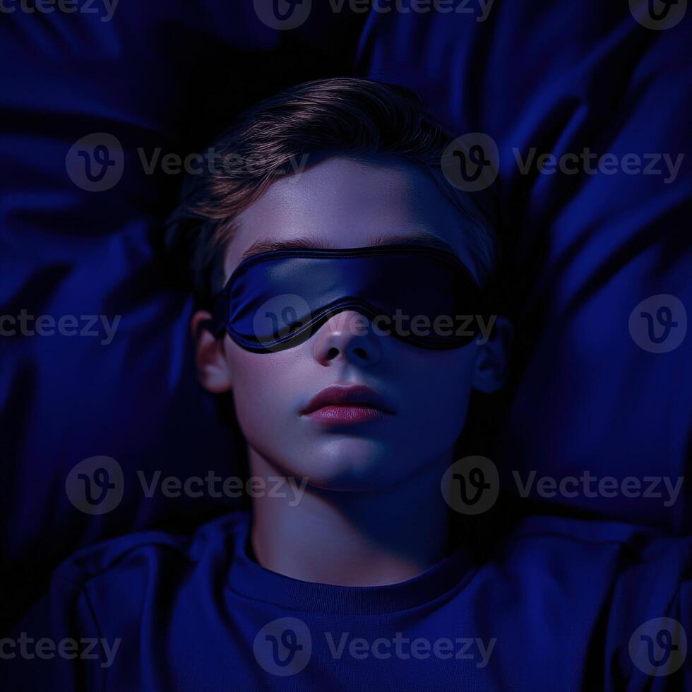 Boy resting peacefully with sleep mask in a dark blue bedroom photo
