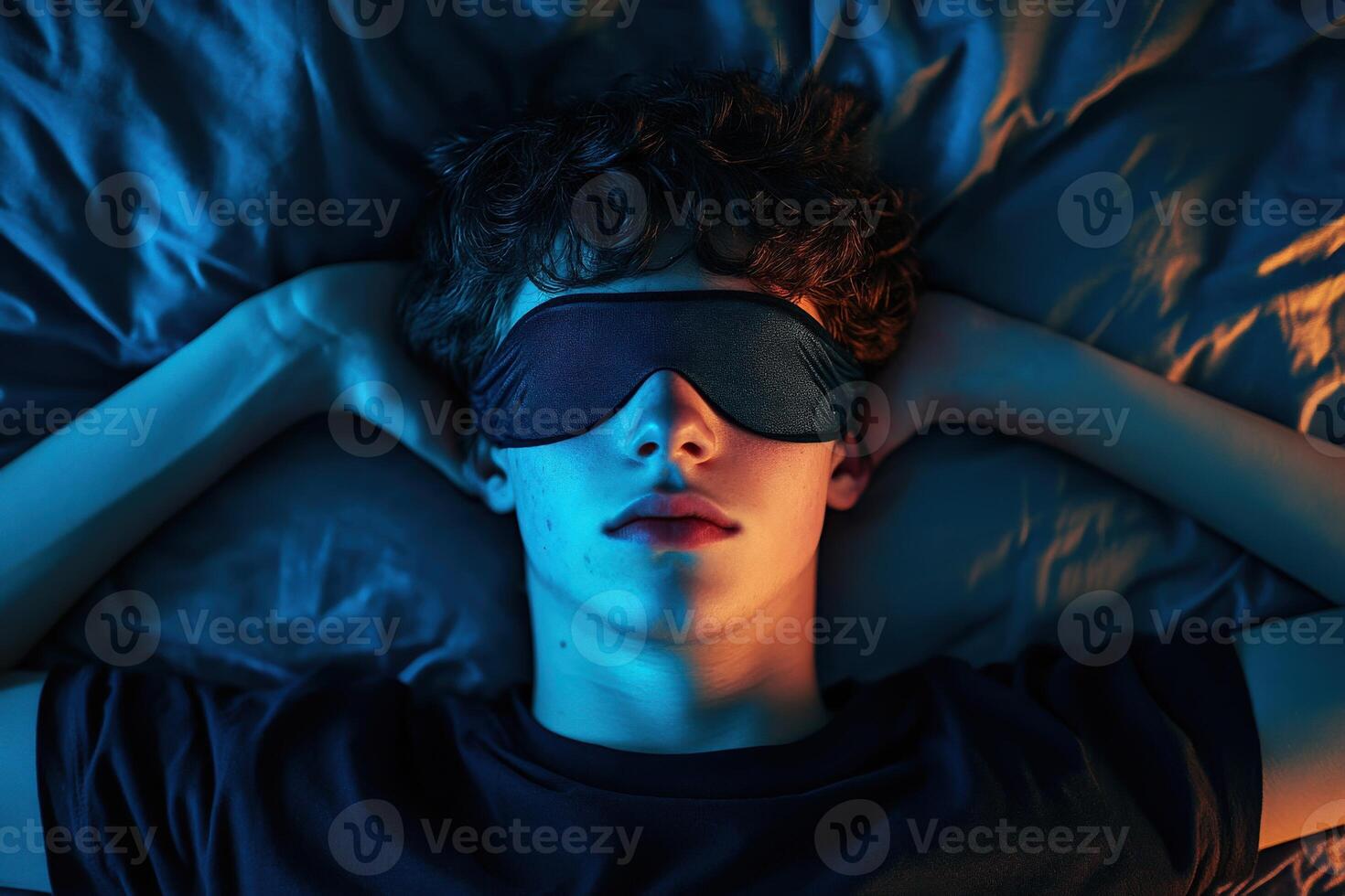 Young man resting with sleep mask on bed in dim light at night photo