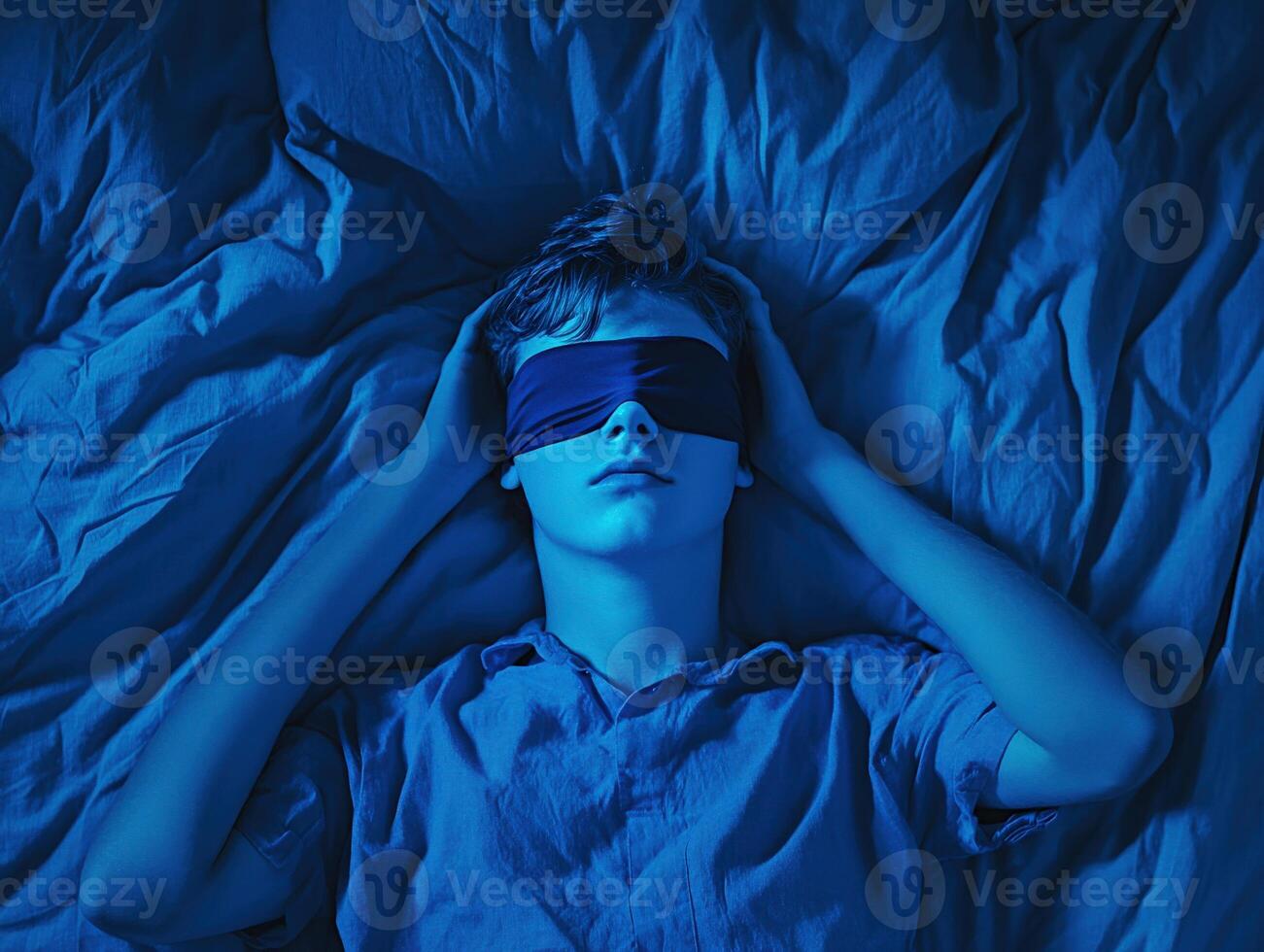 Young boy resting under blue light with a blindfold at home photo
