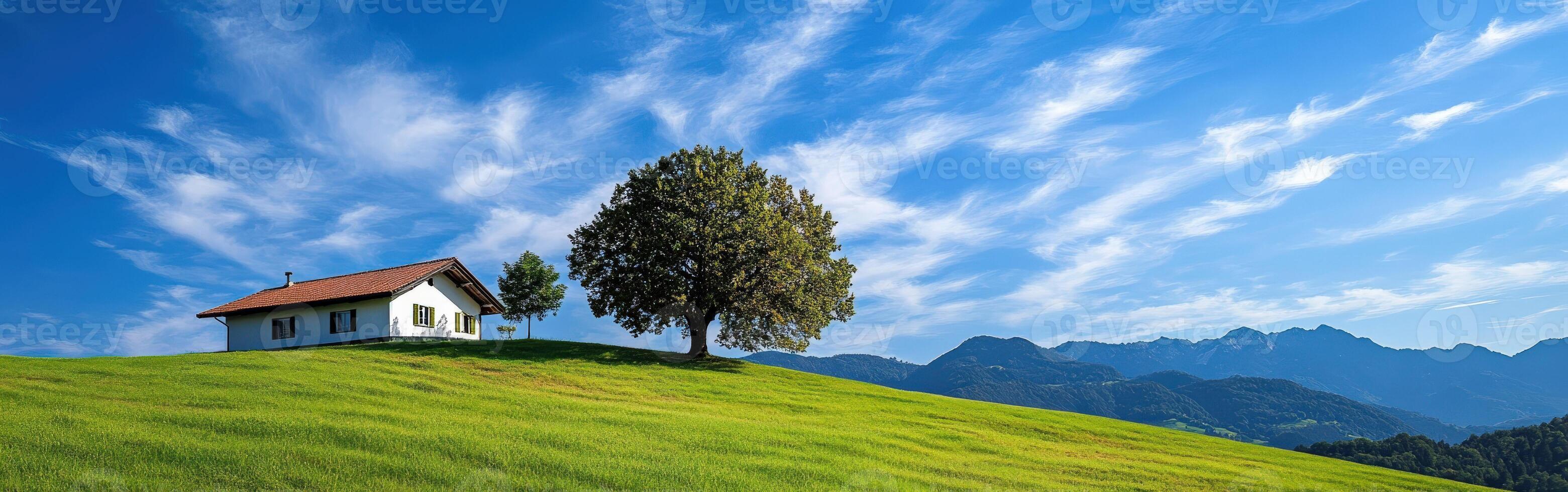 Scenic hillside view with a house and tree under a blue sky photo