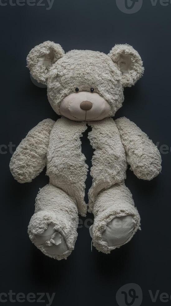 Torn teddy bear laying on a dark surface revealing stuffing inside photo