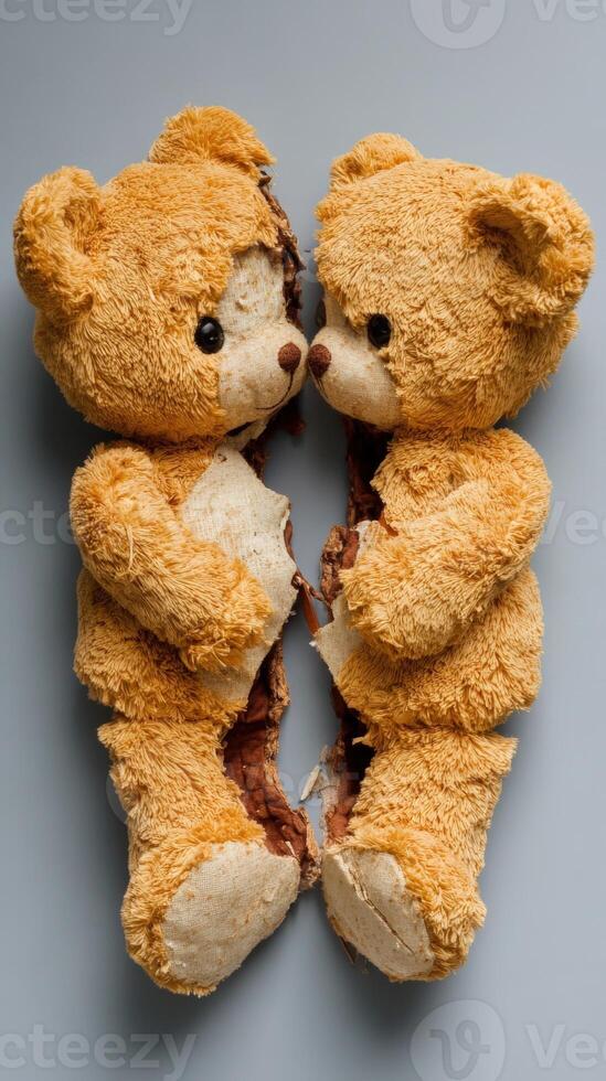 Two torn teddy bears facing each other on a gray surface photo