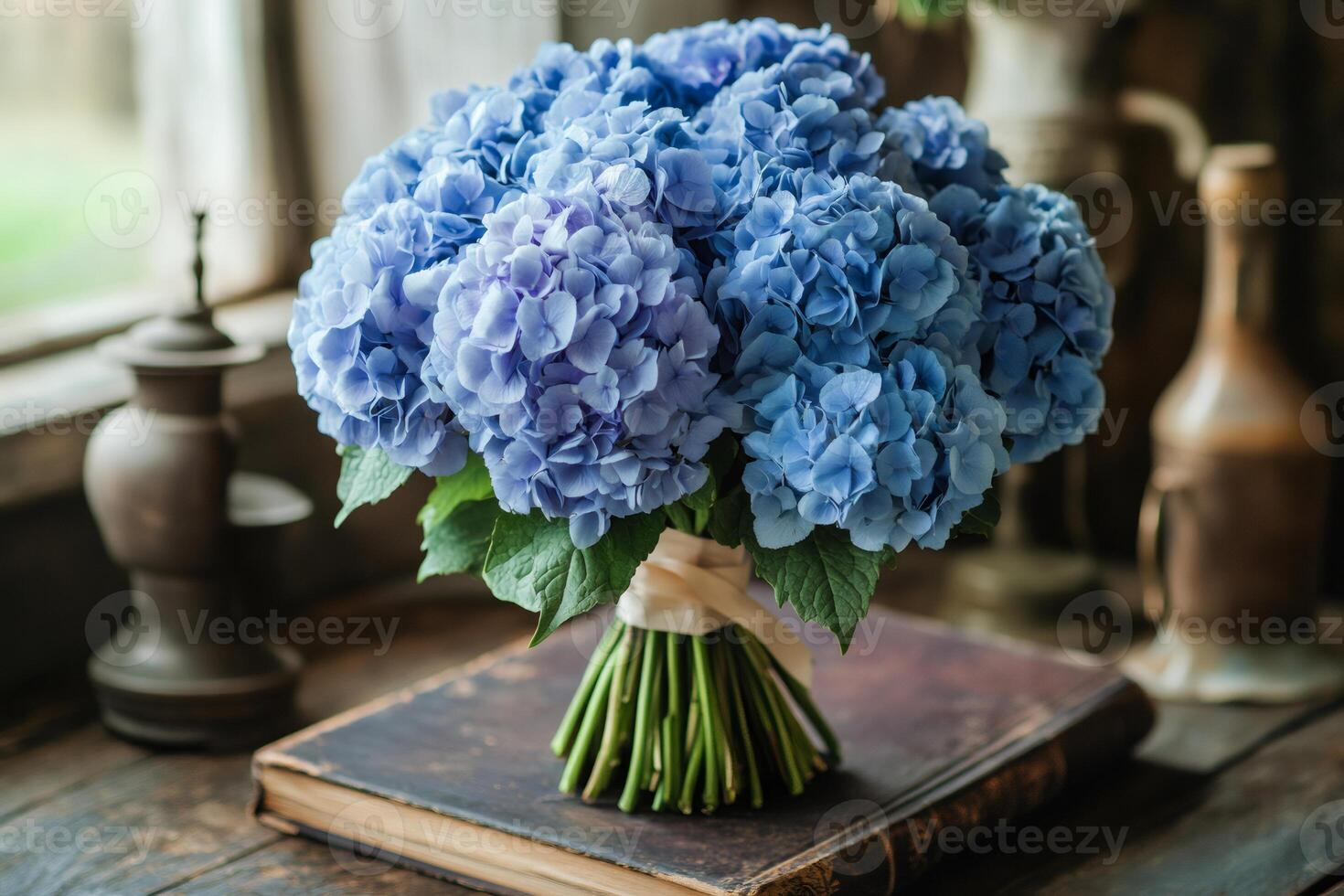 Bouquet of blue hydrangeas lying on antique book near window photo