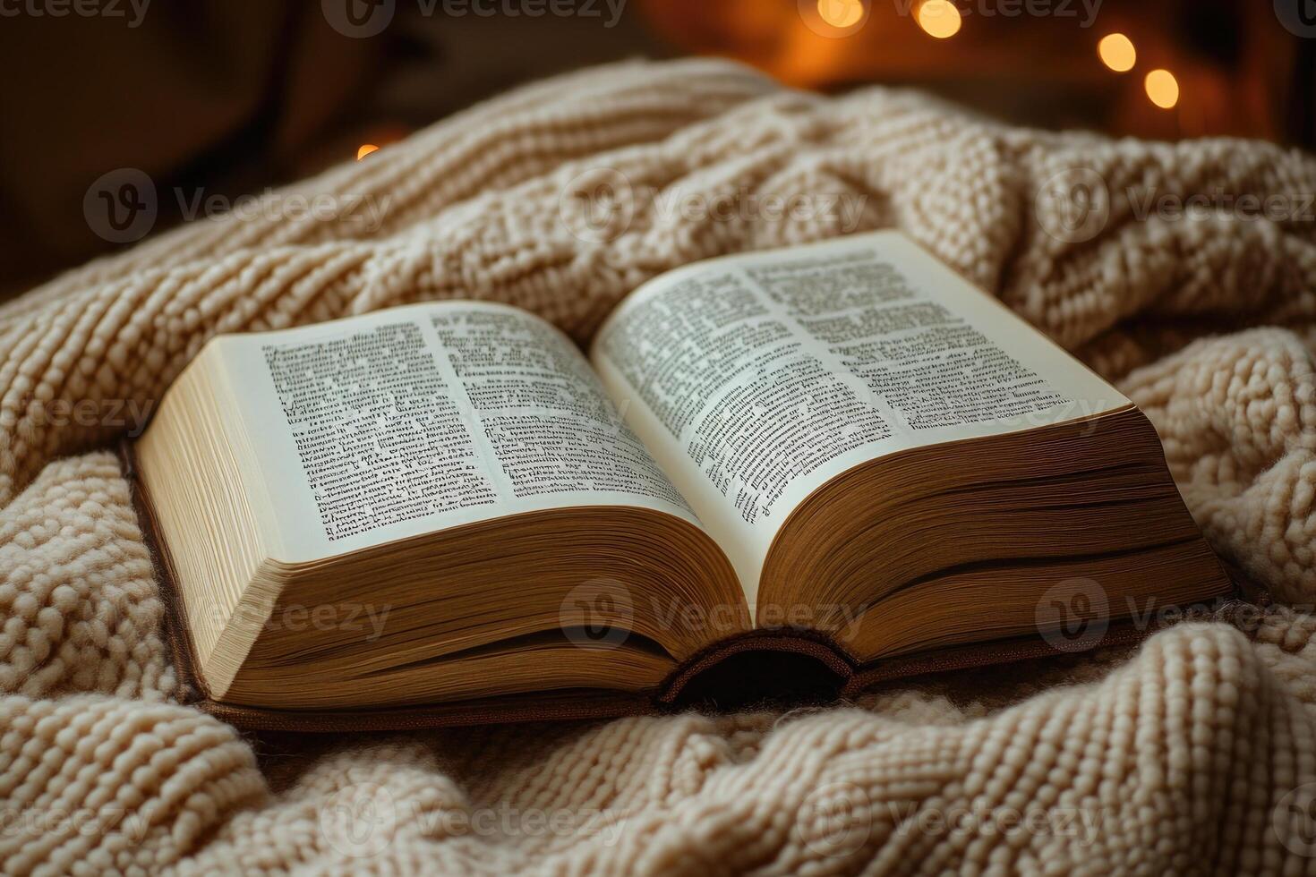 Open book resting on cozy knitted blanket by candlelight photo