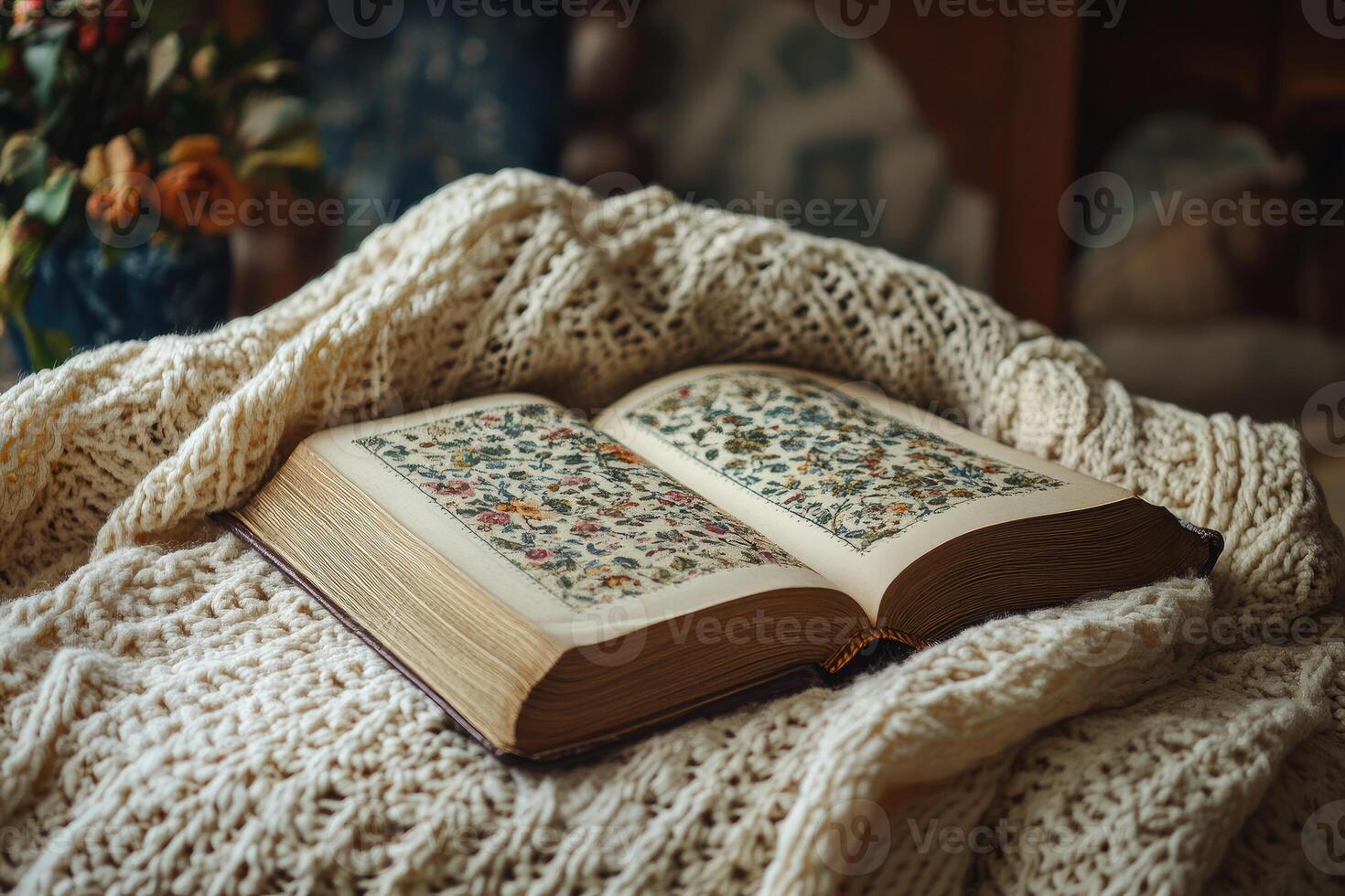 Open antique book showing embroidered flower patterns resting on knitted blanket photo