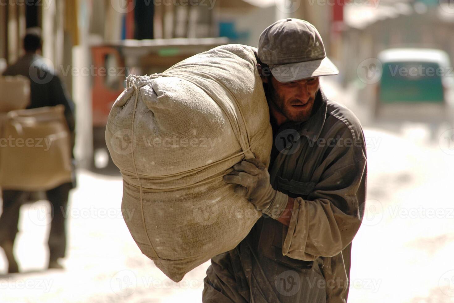 A man carrying a large bag of cement on his back photo