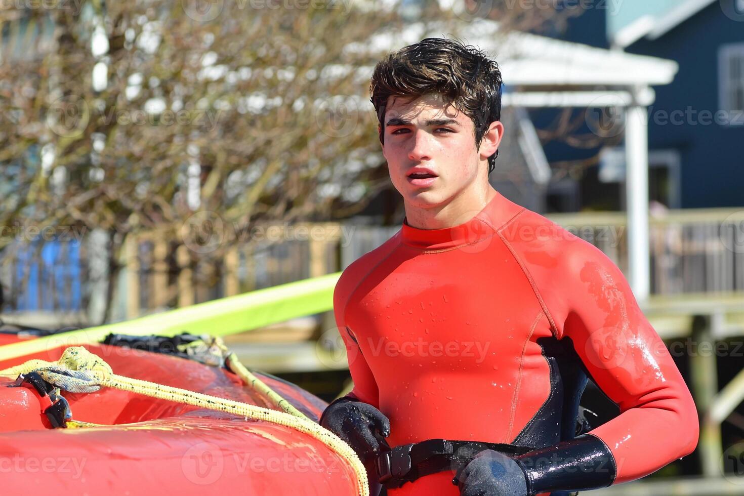 A man in a red wet suit standing next to a red boat photo