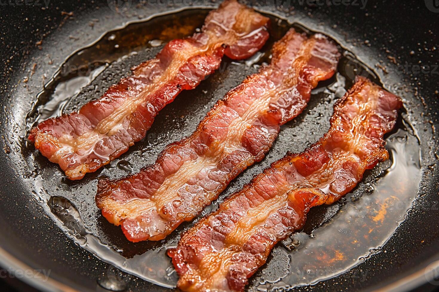 Three pieces of bacon are cooking in a frying pan photo