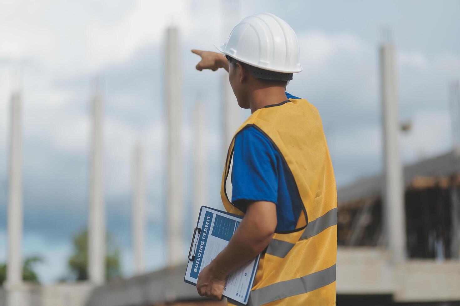 Asian engineer handsome man or architect looking forward holding paperwork blueprint with white safety helmet in construction site. Standing at modern building. photo