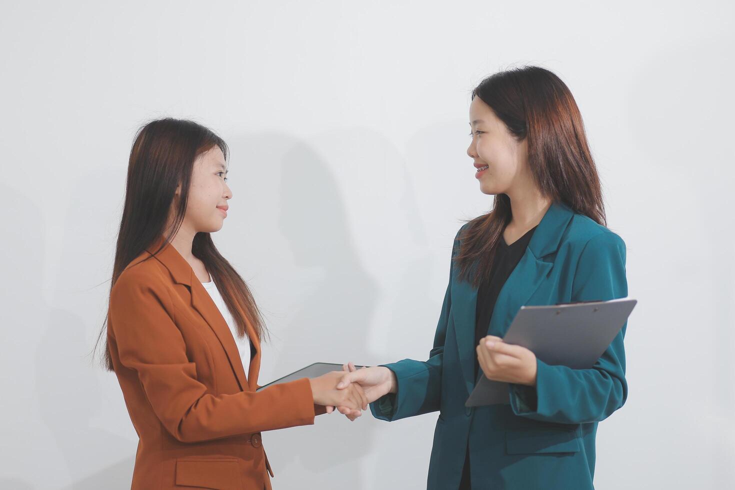 Two Caucasian businesswomen work together using a tablet in a modern office setting, with colleagues engaged in diverse tasks in the background. photo