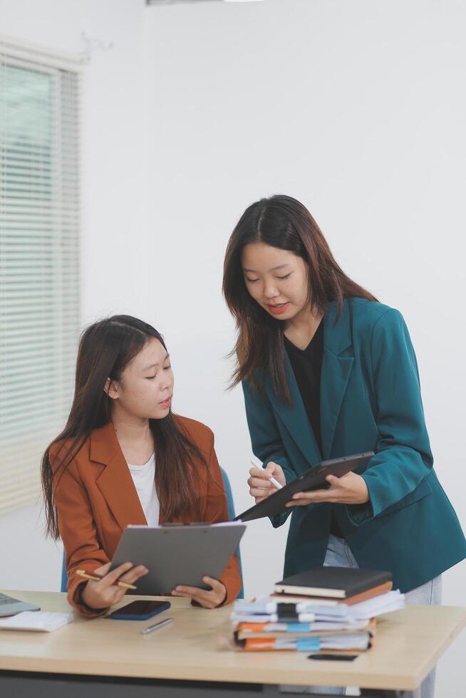 Two young Asian businesswoman discuss investment project working and planning strategy. Business people talking together with laptop computer at office. photo