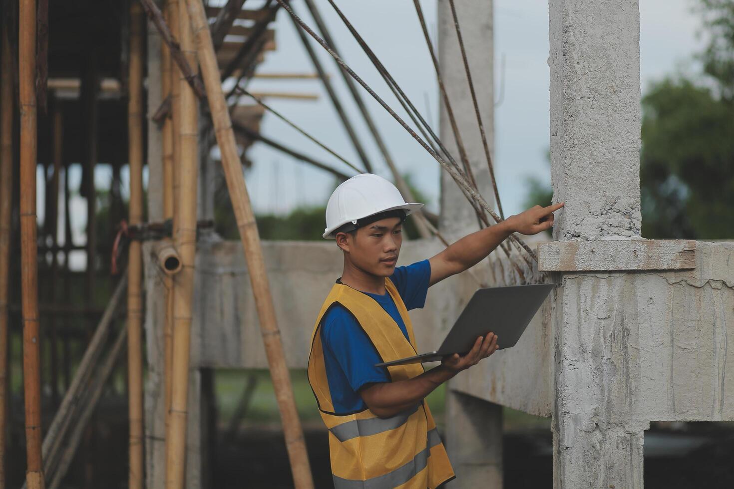 Young handsome asian civil engineer holding tablet looking forward and thinking, planning on construction building background. Evolution construction concept. photo