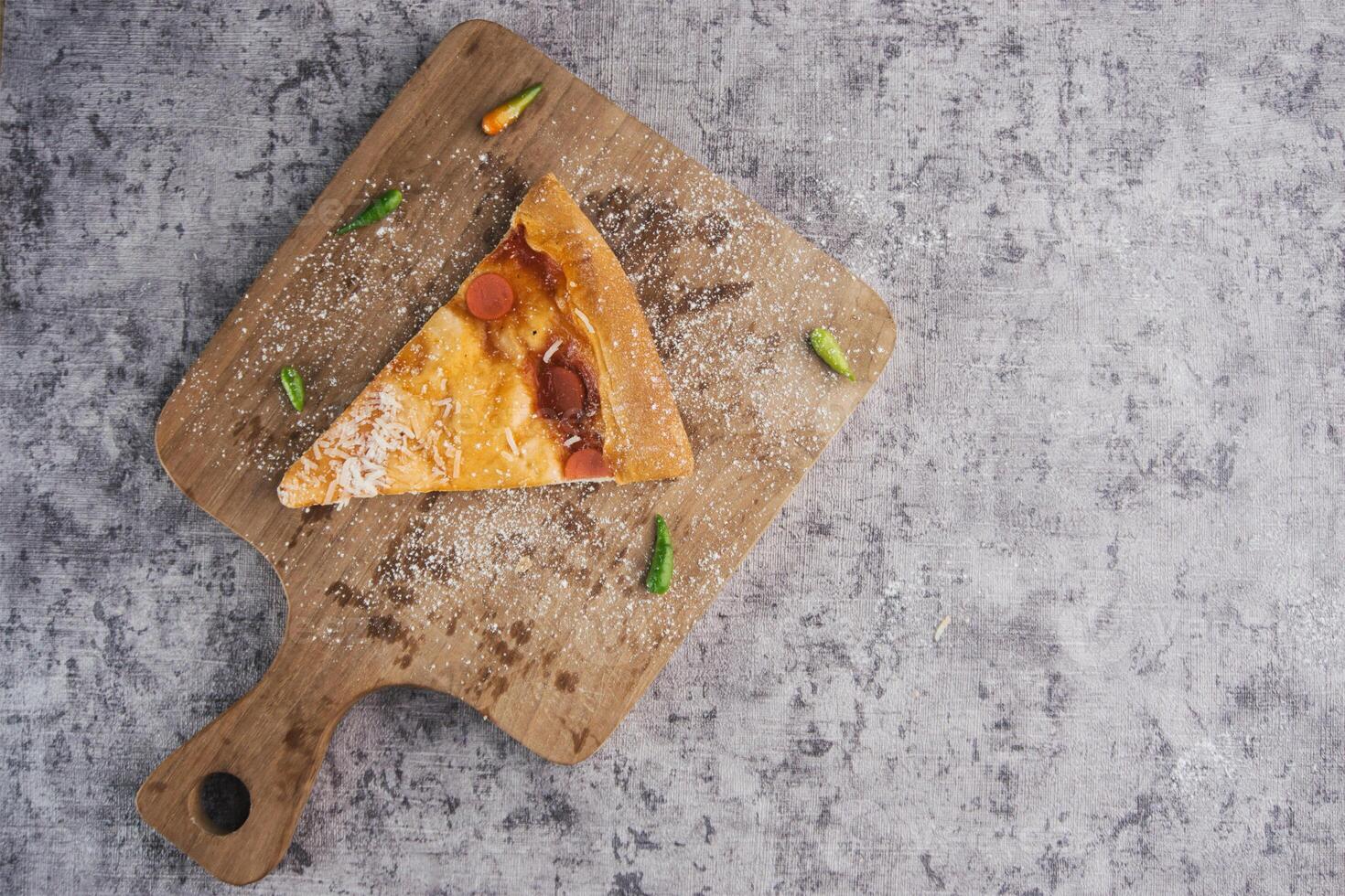 Slice of Pizza on Wooden Board with Parmesan and Fresh Chilies Around photo