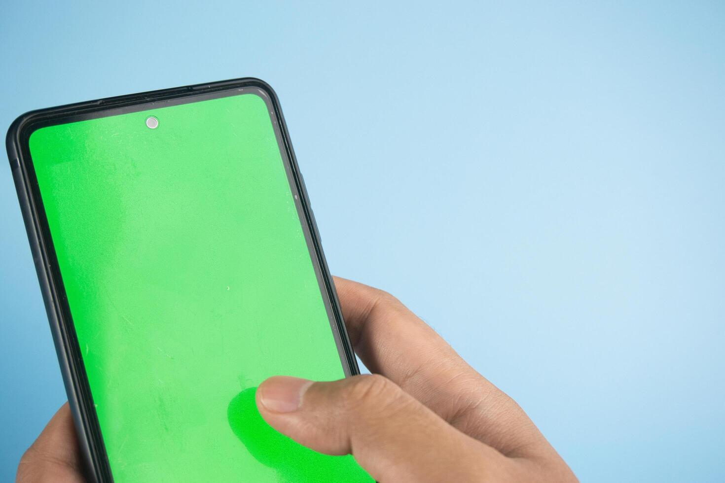 Hand Holding Smartphone With Green Screen on Blue Background photo