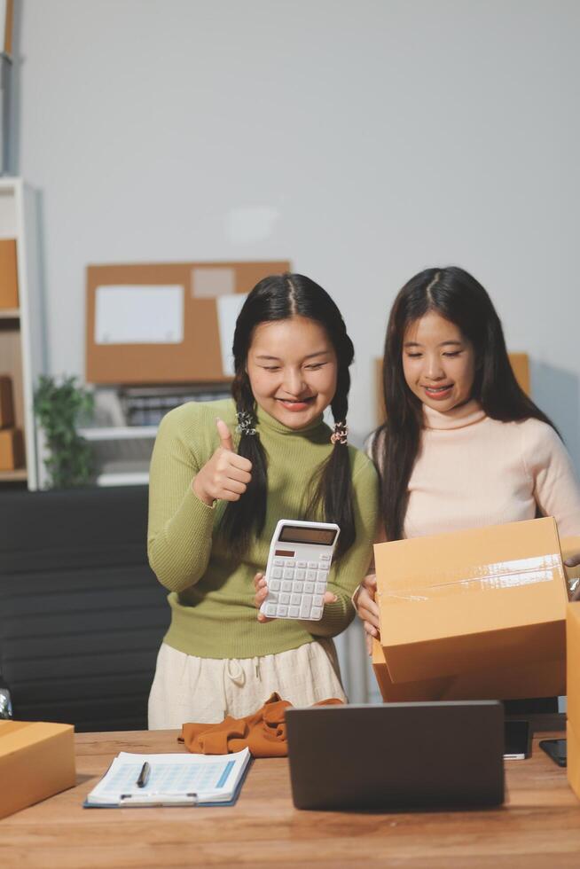 Startup SME small business entrepreneur of freelance Asian woman wearing apron using laptop and box to receive and review orders online to prepare to pack sell to customers, online sme business ideas. photo