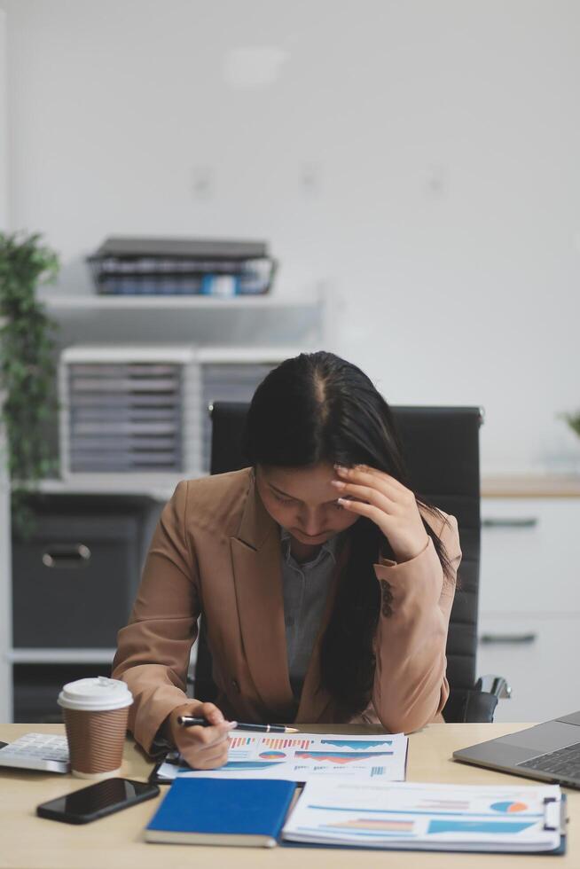 Portrait of tired young business Asian woman work with documents tax laptop computer in office. Sad, unhappy, Worried, Depression, or employee life stress concept photo