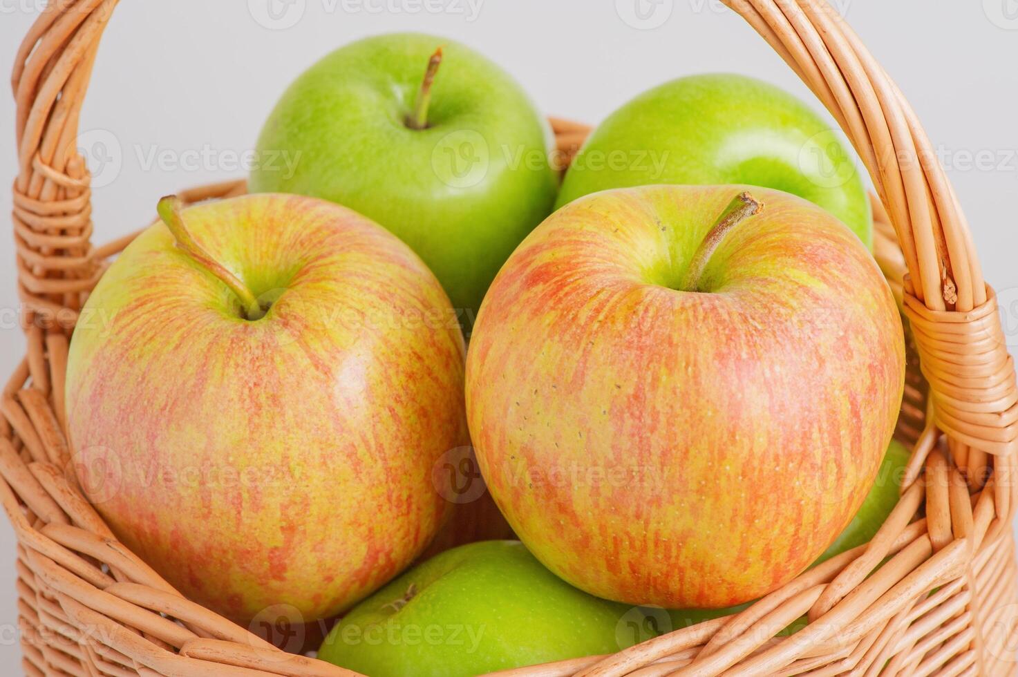 Two different varieties of apples in a wicker basket on a gray background. Fruits, apples. photo