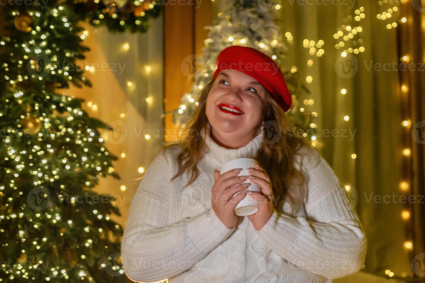 Woman Christmas Lights Holiday Cheer - A woman in a red beret is smiling while holding a cup of coffee and standing in front of a Christmas tree with lights. photo
