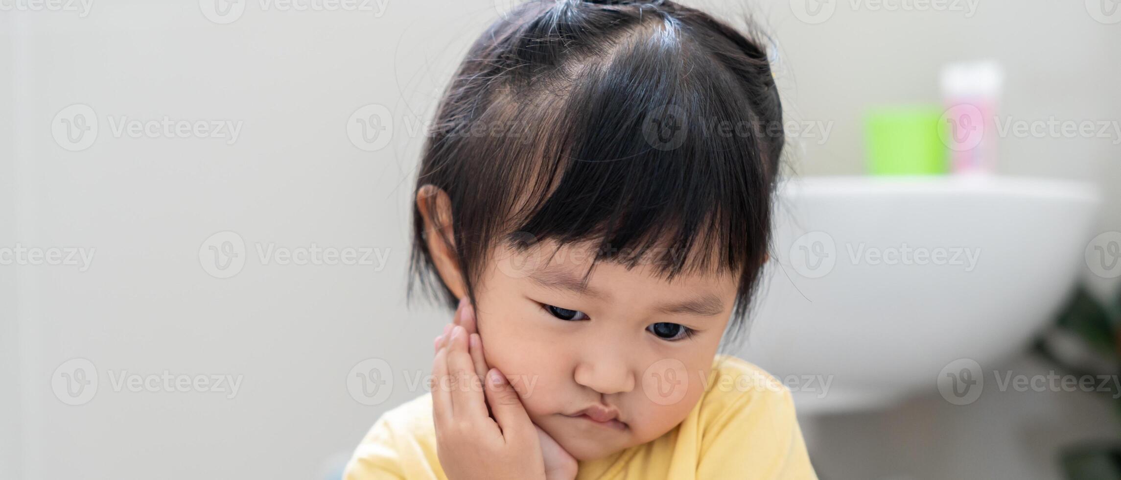 little asian girl presses hand to cheek, suffers from pain in tooth. Teeth decay, dental problems, child emotions and facial expression, oral health care, reducing sweets, fluorine coating photo