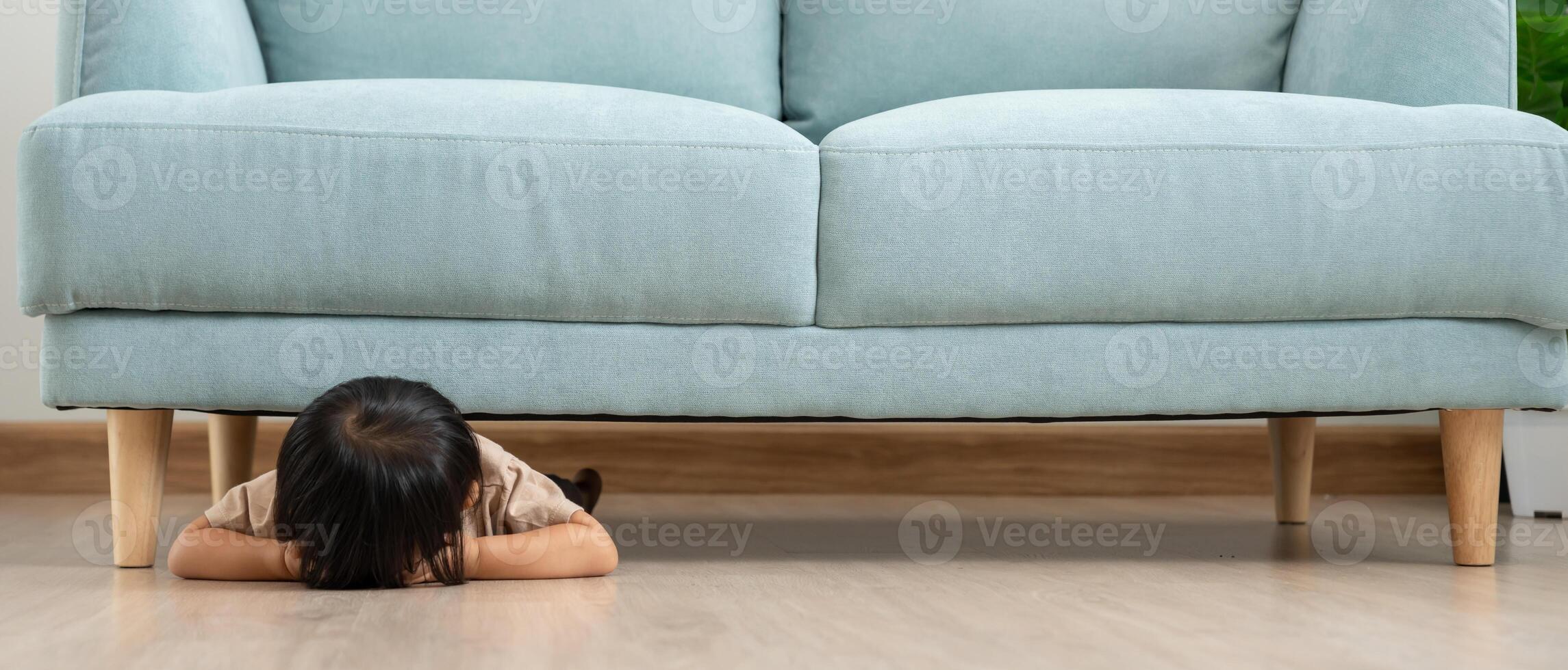 little asian children kid playing hide and seek behind the sofa, Adorable child having fun in the home. happy family have fun with kids, activity, learning, activity, game, meditation photo