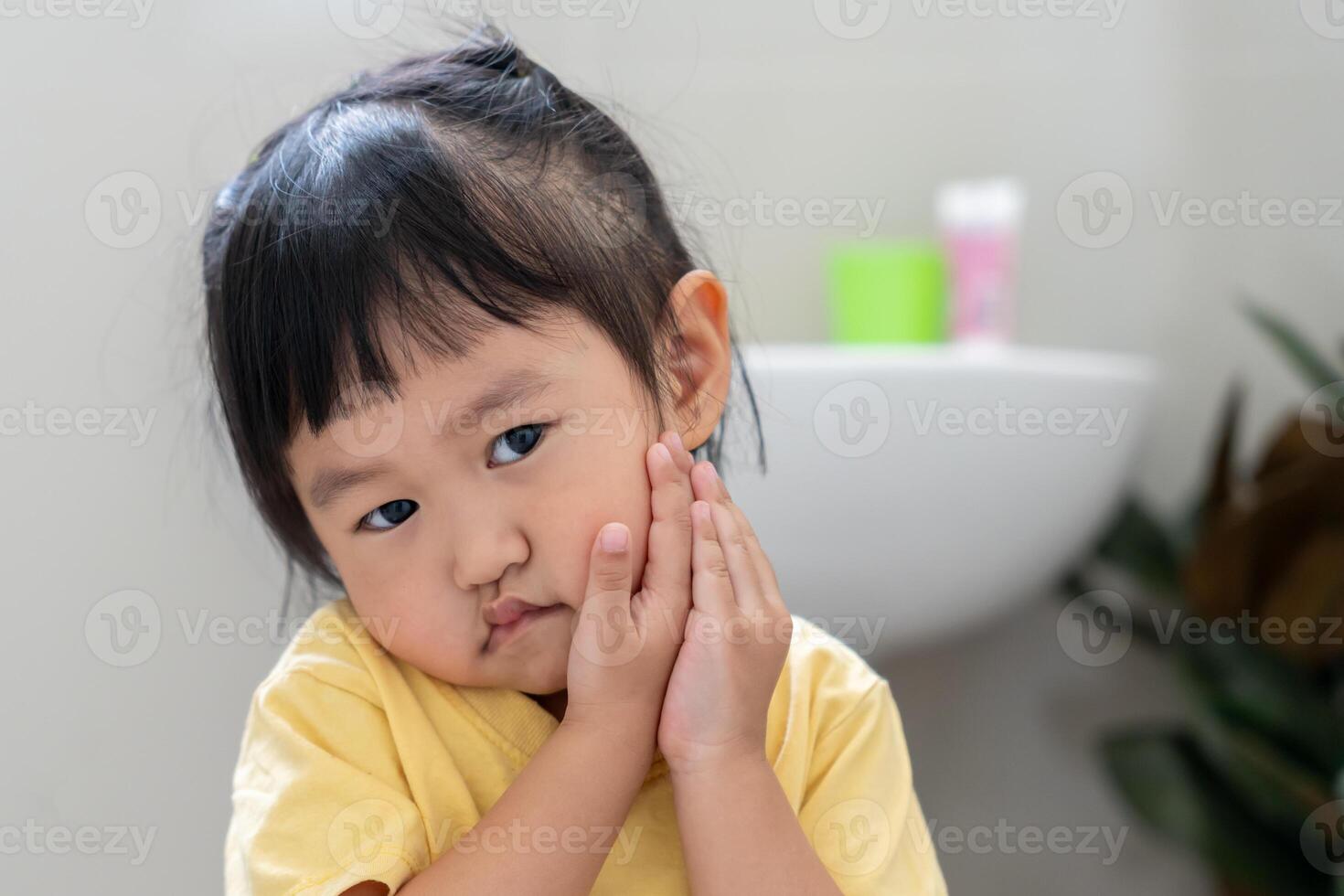 little asian girl presses hand to cheek, suffers from pain in tooth. Teeth decay, dental problems, child emotions and facial expression, oral health care, reducing sweets, fluorine coating photo