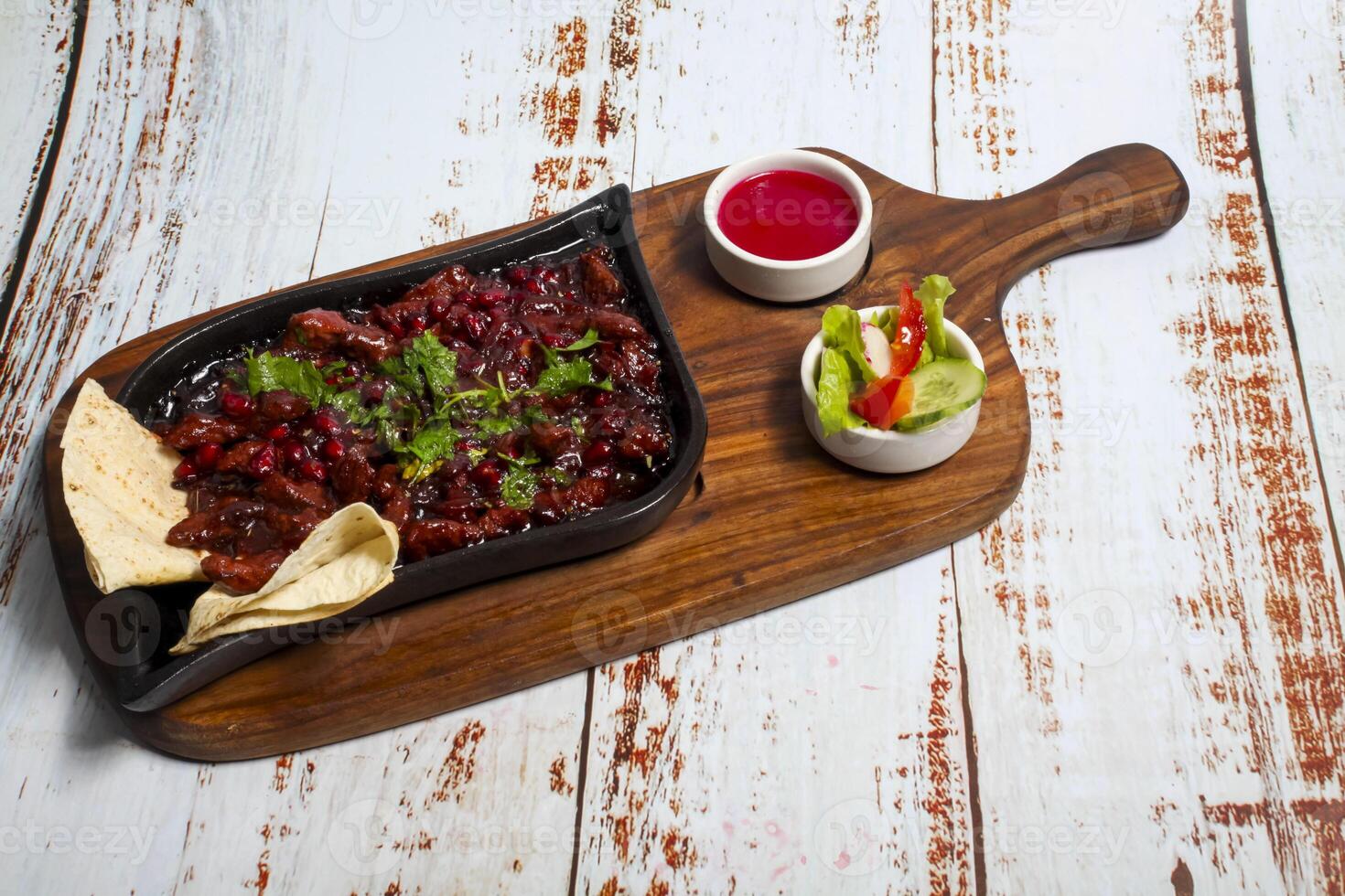 Sizzling dish served on a wooden platter with fresh salad and dipping sauce photo