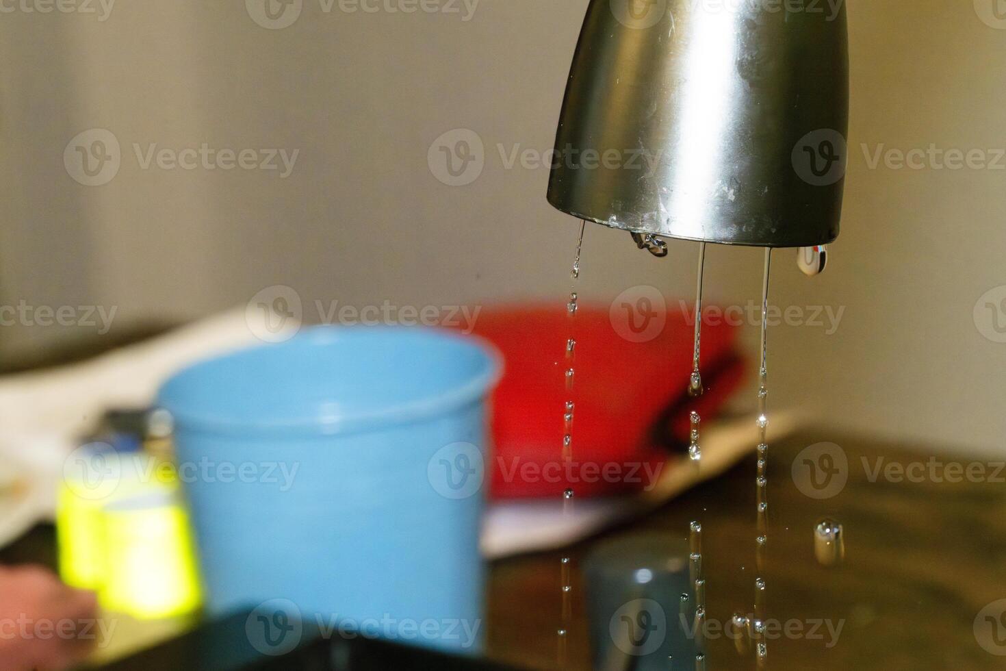 Water dripping from a kitchen faucet into a blue bucket photo