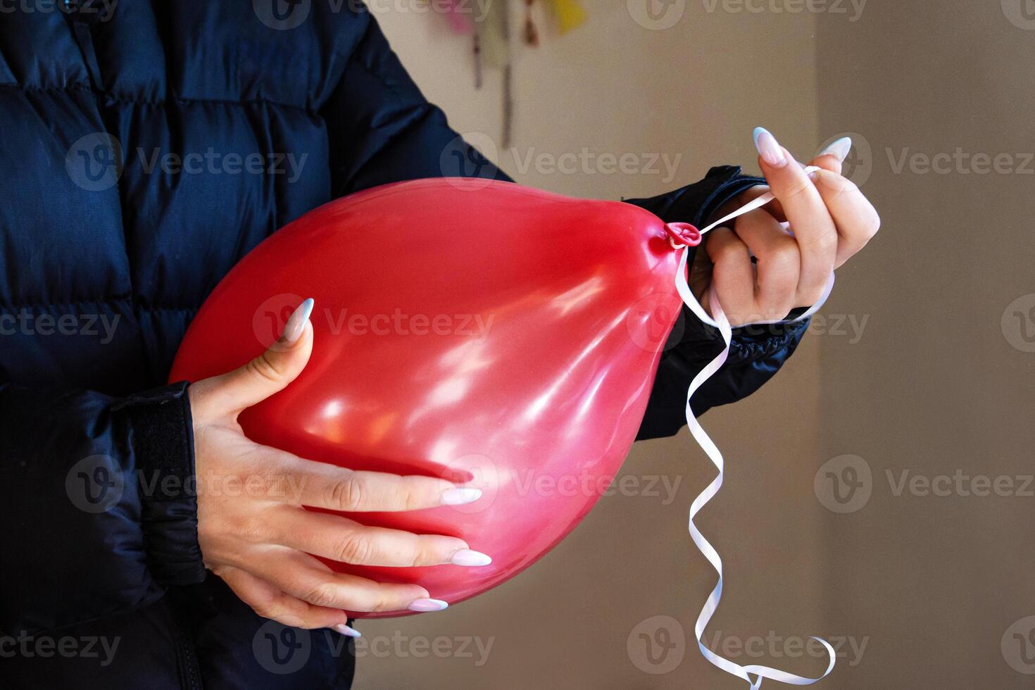Closeup of woman hands tying ribbon on a red balloon for a party decoration. Person holding a balloon with curly ribbon during birthday party preparations. photo