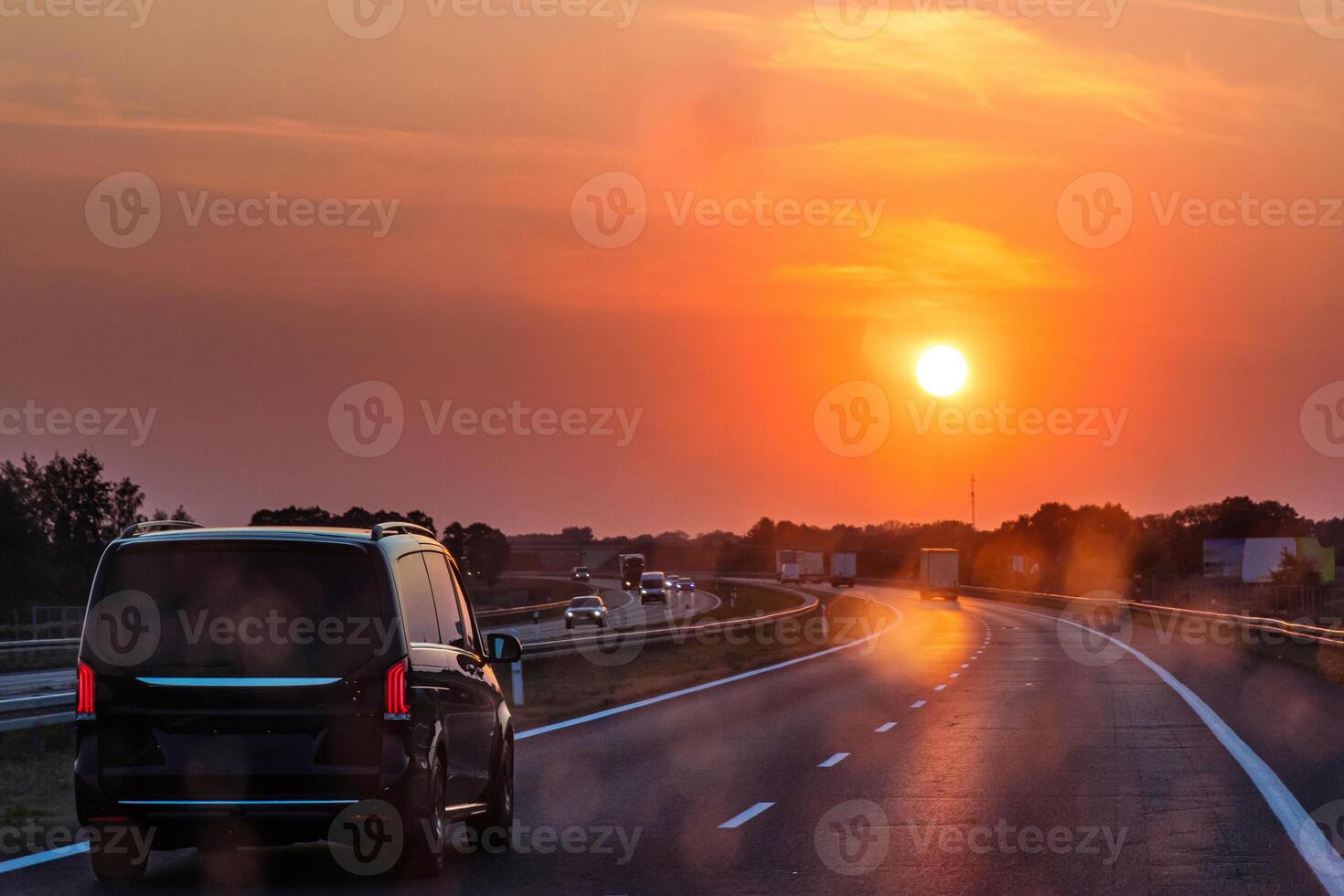 Scenic highway at sunset with minivan and cars and trucks driving through a dirty windshield. Concept of travel, transportation, freedom and the beauty of evening skies on the open road. Copy space photo