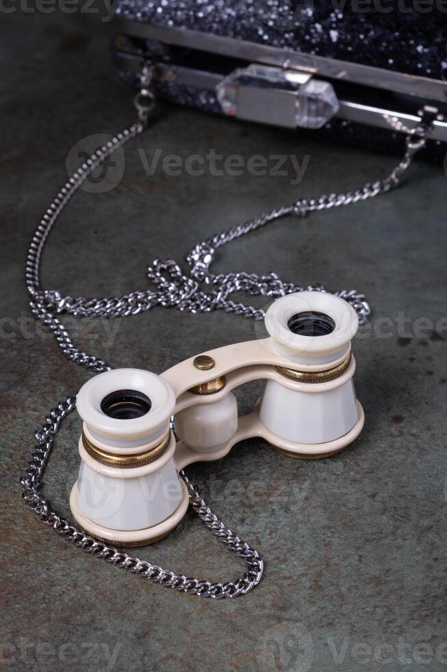 Vintage opera glasses with a black clutch are elegantly displayed. Nostalgia and luxury. photo