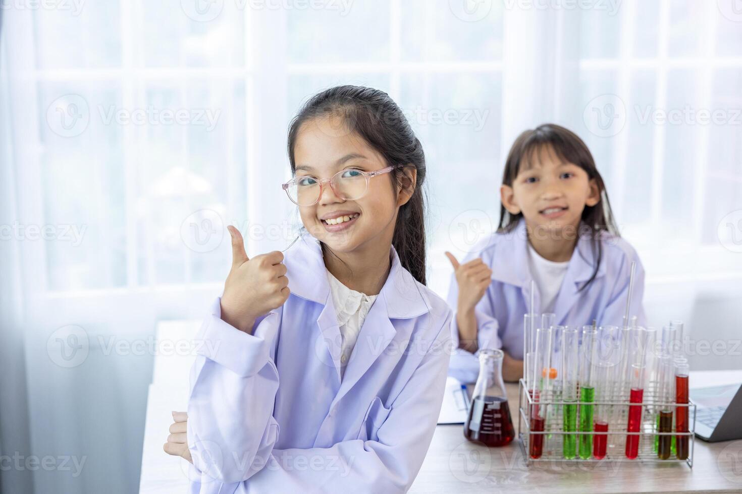 Two young asian students in scientific lab gown while studying science lesson in the classroom for education, literacy and tutoring concept with copy space photo