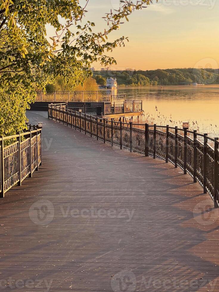Wooden path winding through trees along the river bank at sunset photo