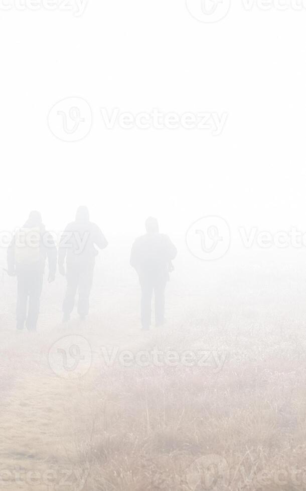 People in fog are walking across the field. Fog on the field photo