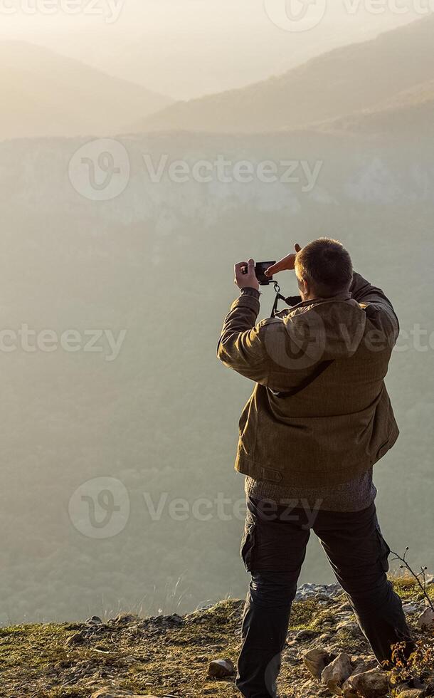 man is on top of the mountain and takes pictures of the landscape of mountains and autumn forest. photo