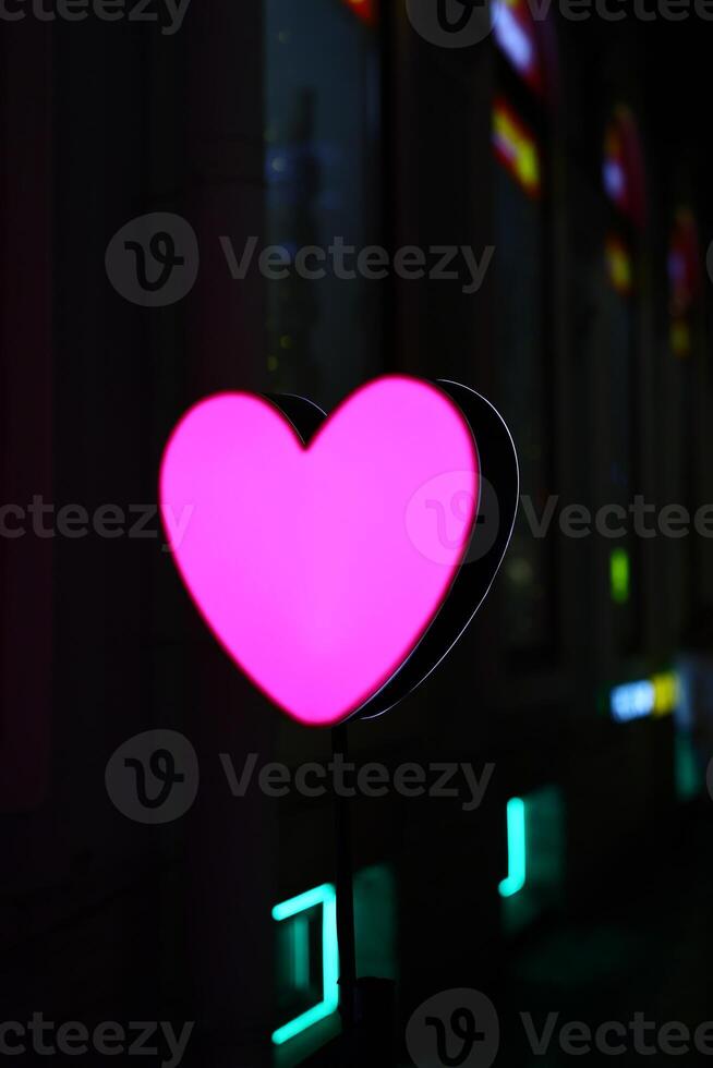 A stunningly vibrant pink heart neon sign captivatingly placed within an urban city environment photo