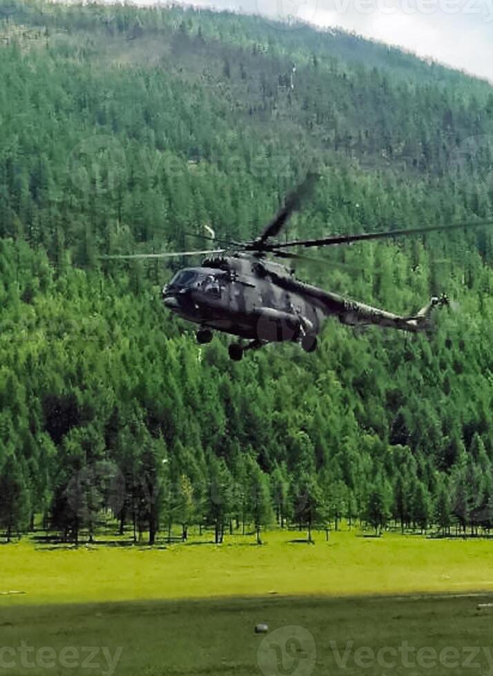 Helicopter MI-8 lands on edge in the woods in mountains. photo