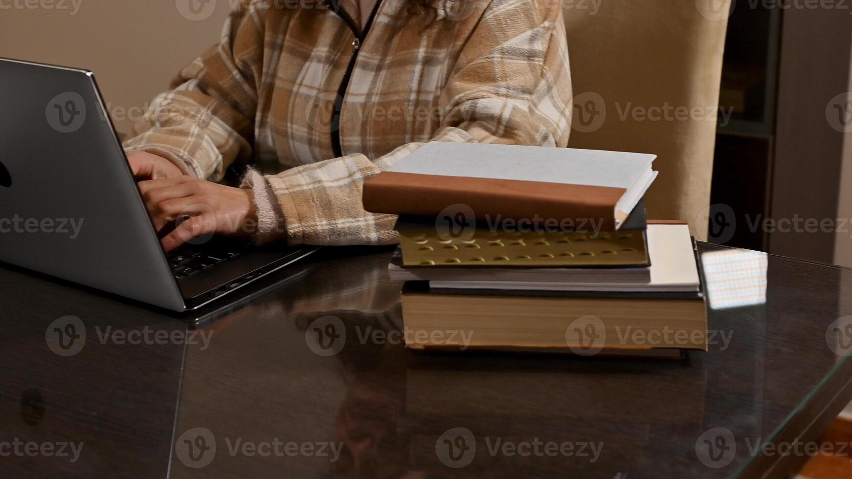 Person Working on Laptop at Office Desk with Books Nearby photo