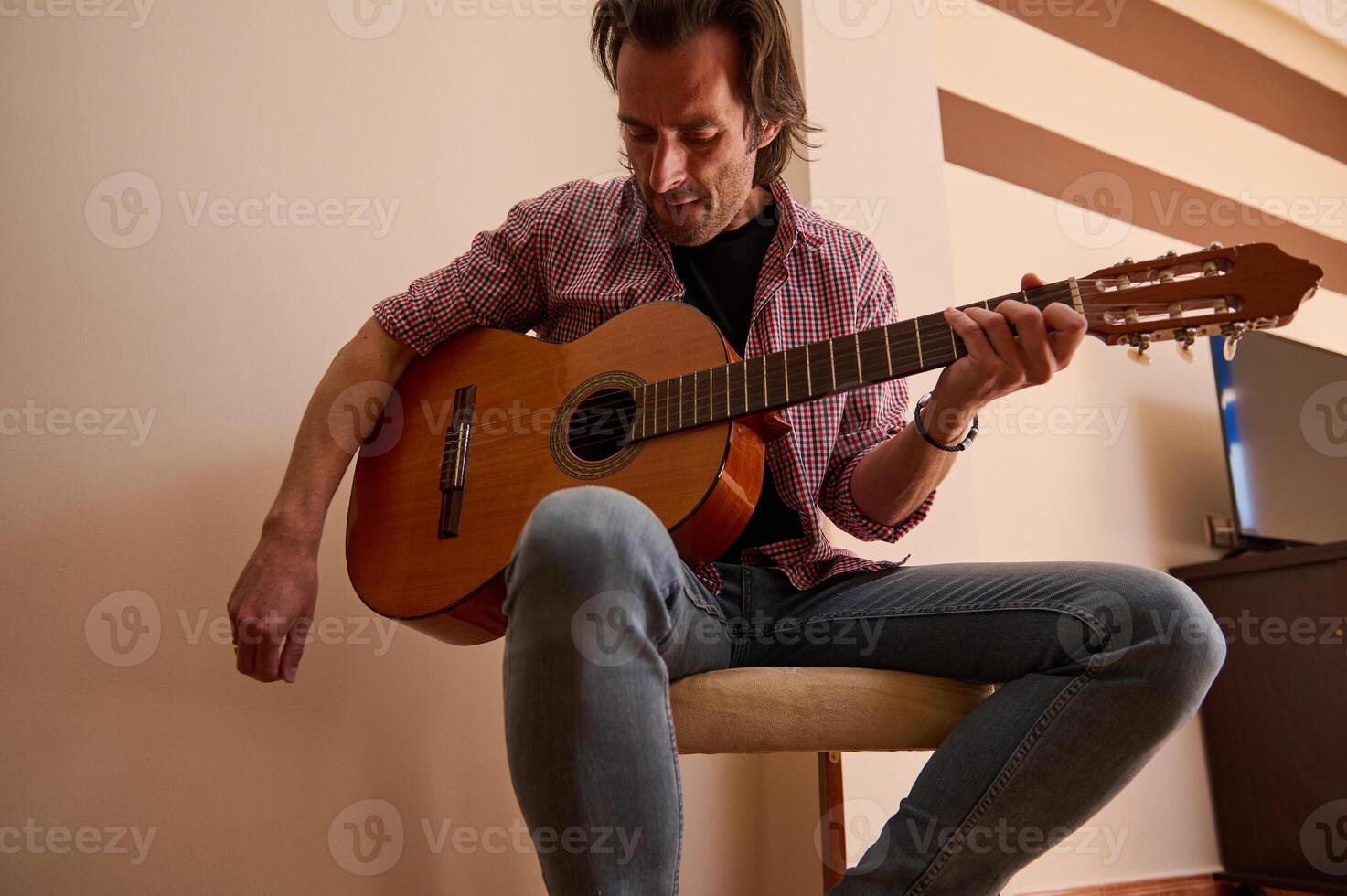 Man playing classical acoustic guitar while sitting indoors tuning strings photo