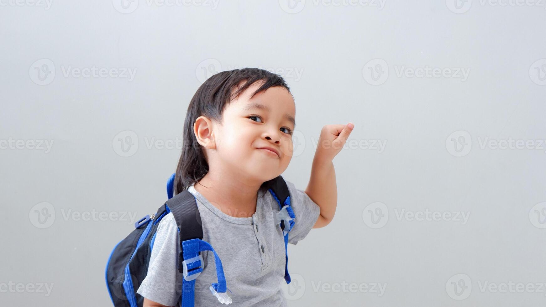 Cute Asian child student with backpack pointing with finger, confident gesture looking serious photo