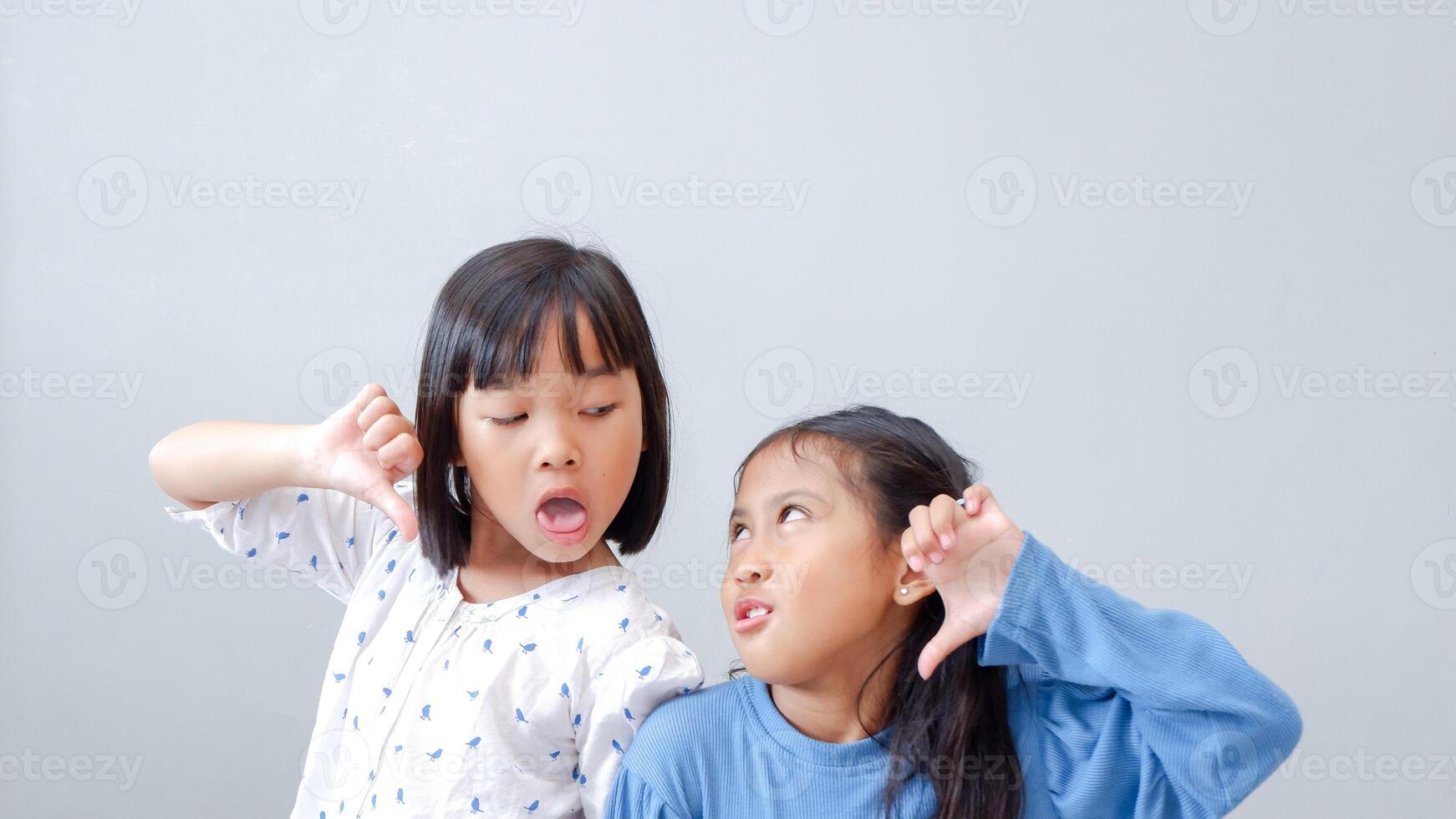 Young girl teasing and mocking a friend - sticking her tongue out, isolated on gray background. photo