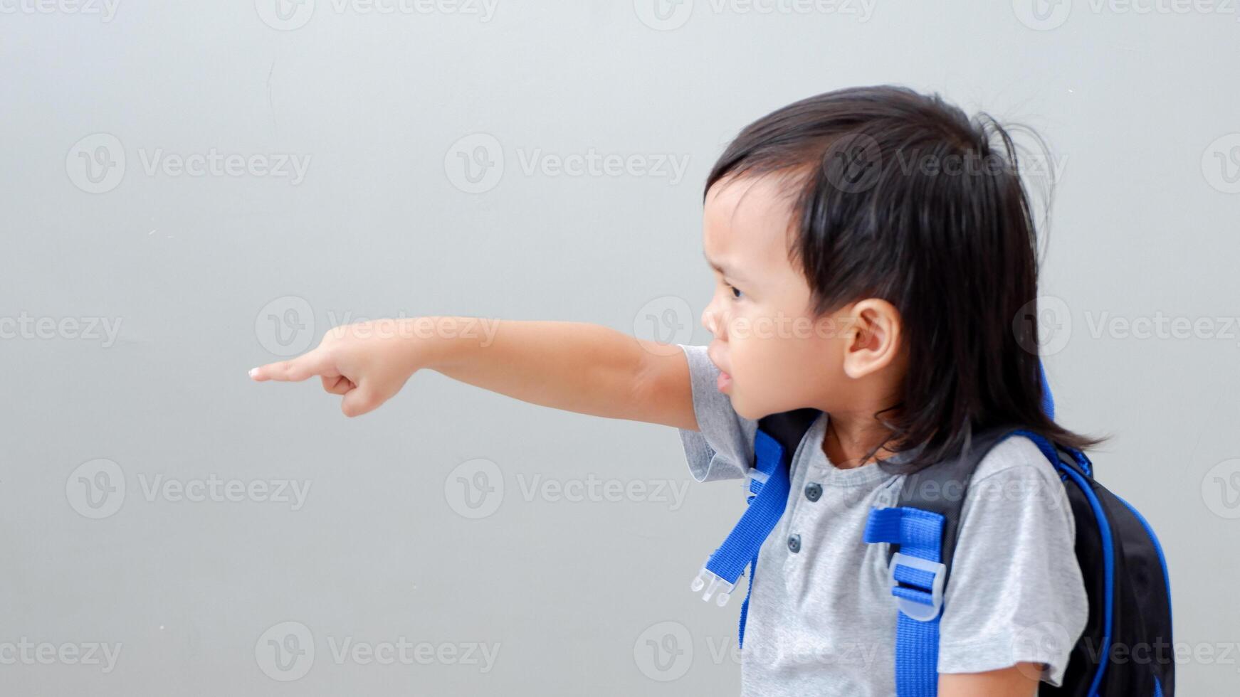 Cute Asian child student with backpack pointing with finger, confident gesture looking serious and mad photo