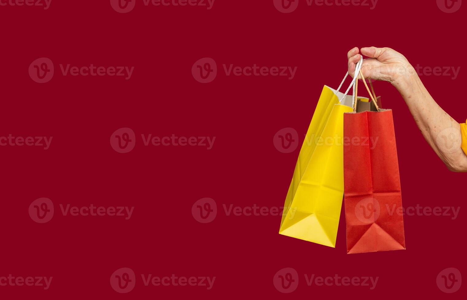 Close-up of hand holding yellow and red shopping bags with a handle while standing on a red background photo