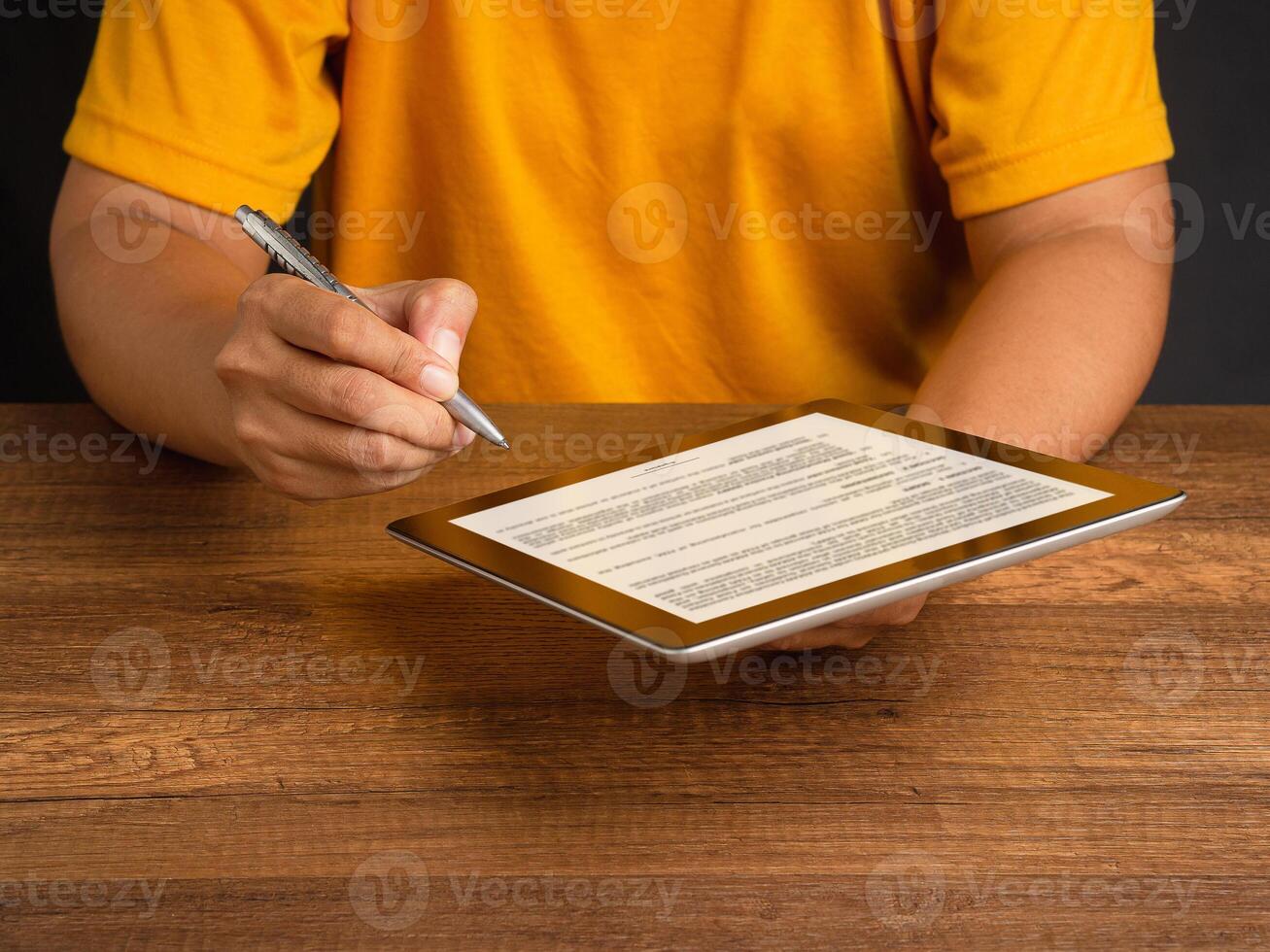 Hand of a man in an orange casual signing on lease contract or agreement on a tablet while sitting at the table photo