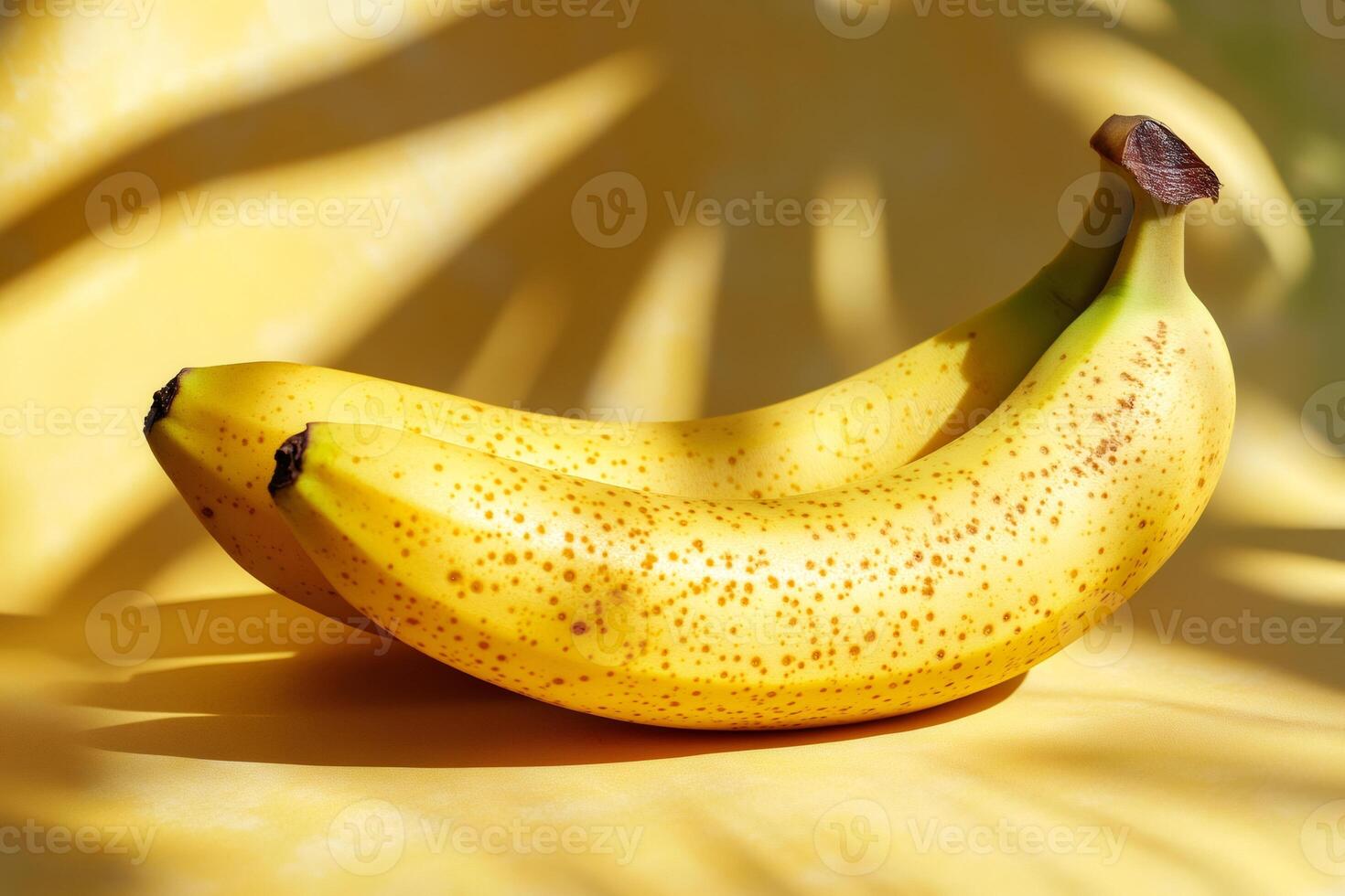 Two ripe bananas resting on yellow surface with leaf shadows photo