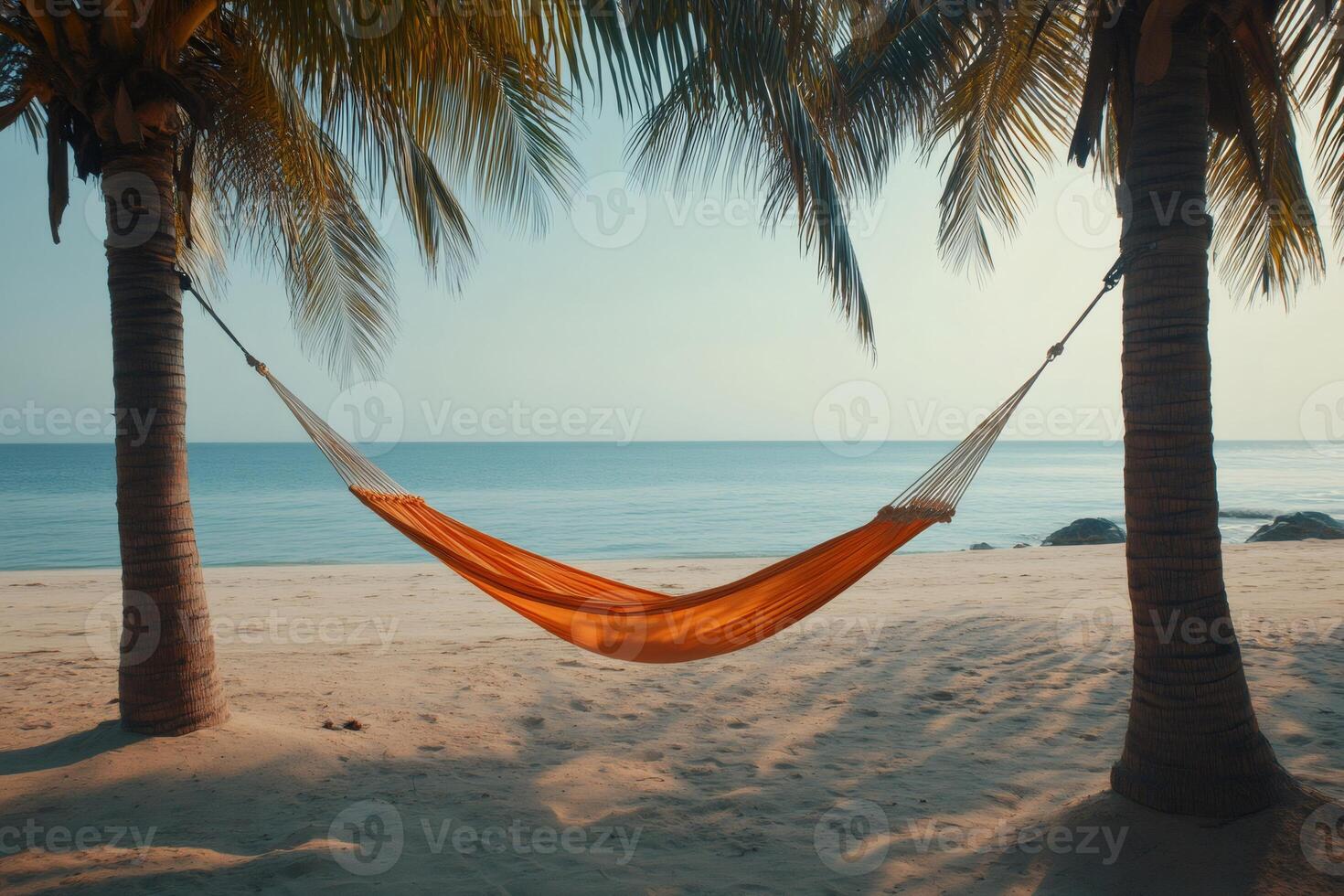 Orange hammock hanging between two palm trees on tropical beach photo