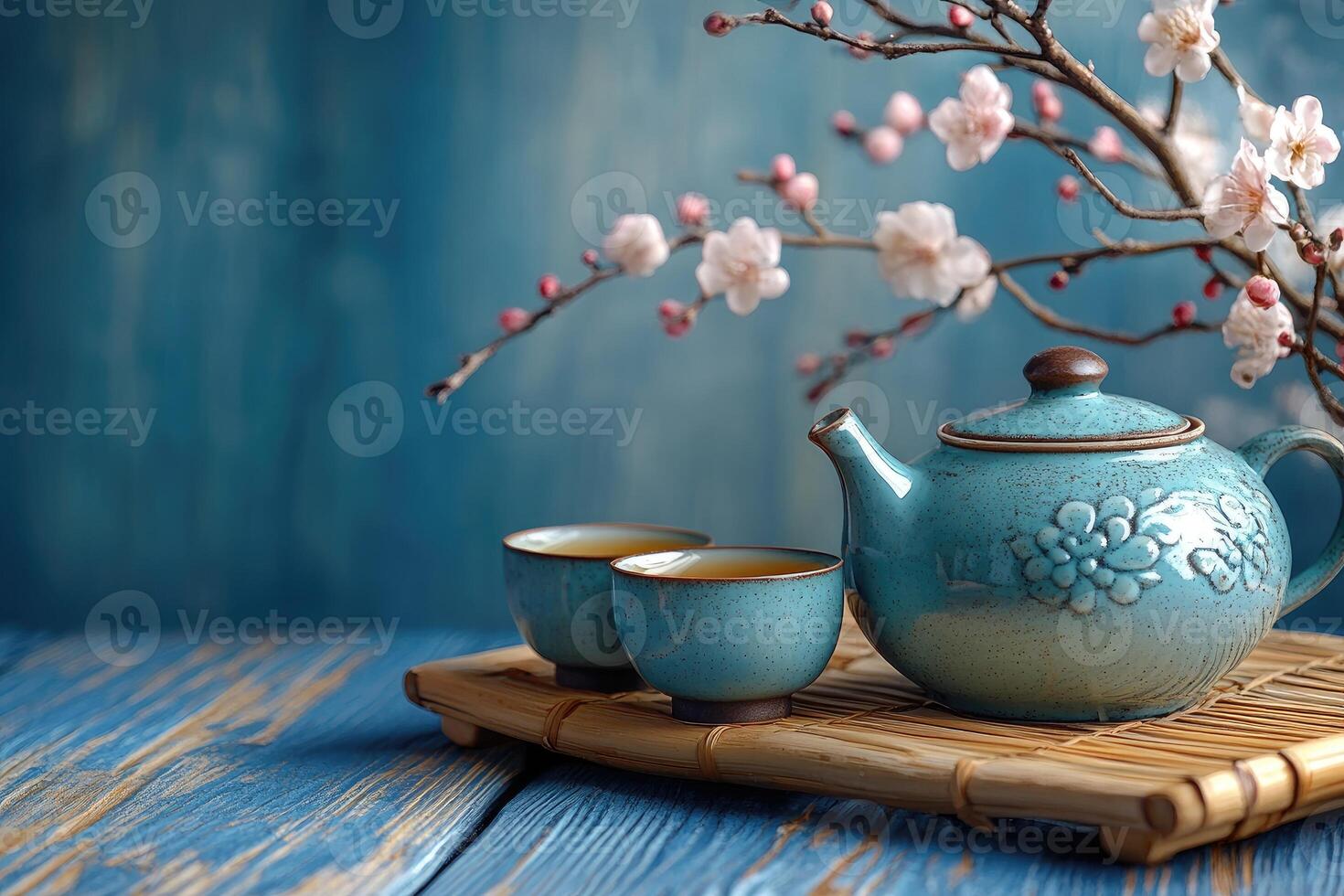 Turquoise teapot and two cups resting on bamboo tray with cherry blossom branch photo