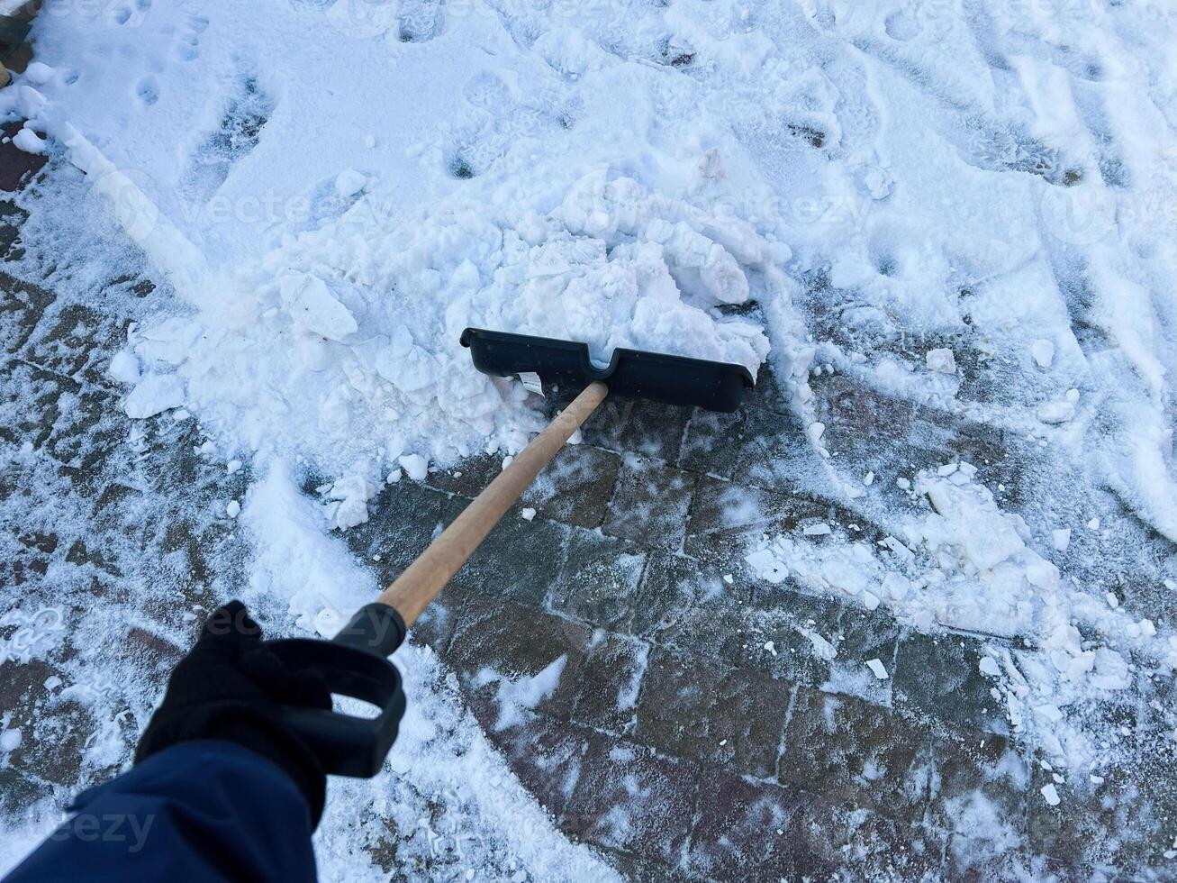 Person shoveling snow from a winter sidewalk with a manual snow shovel photo