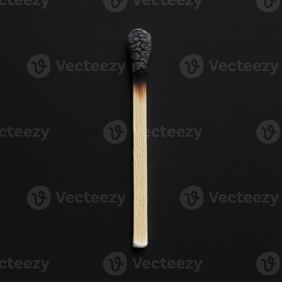 Burned matchstick lies on a black surface showcasing its charred head and wooden shaft illuminated by soft light photo