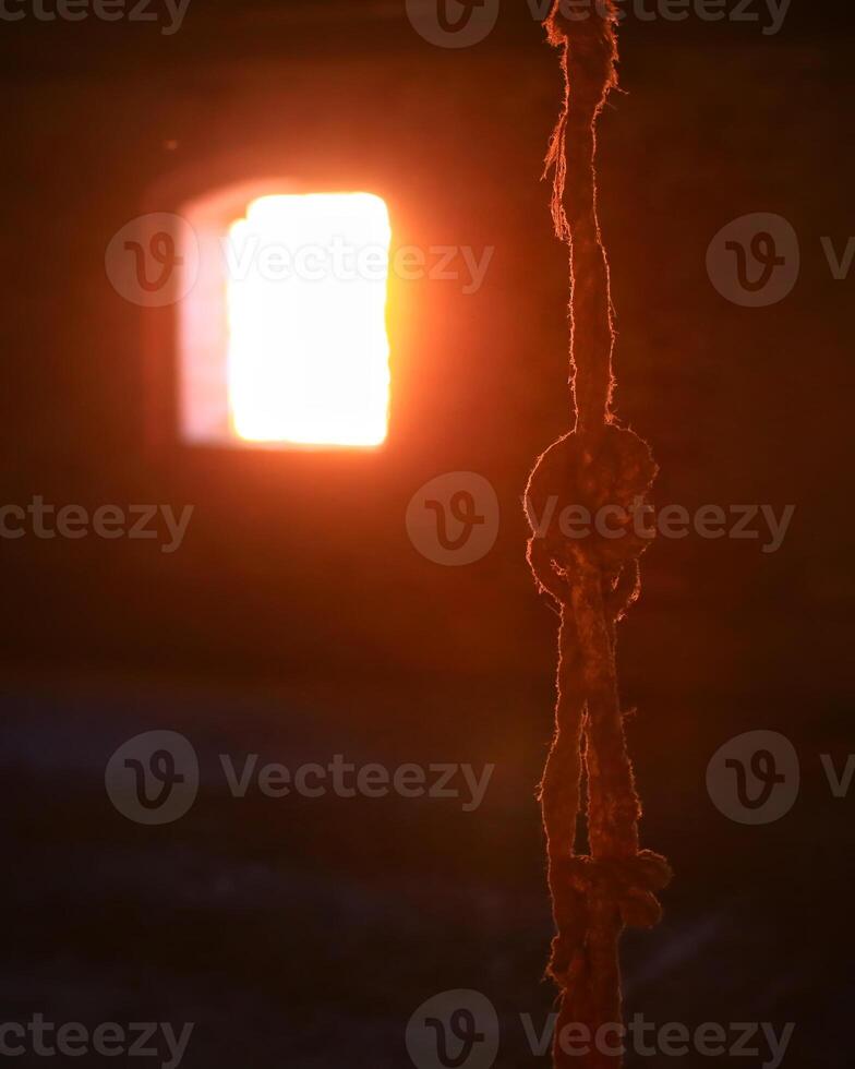 Torn rope hanging in front of bright sunny window photo
